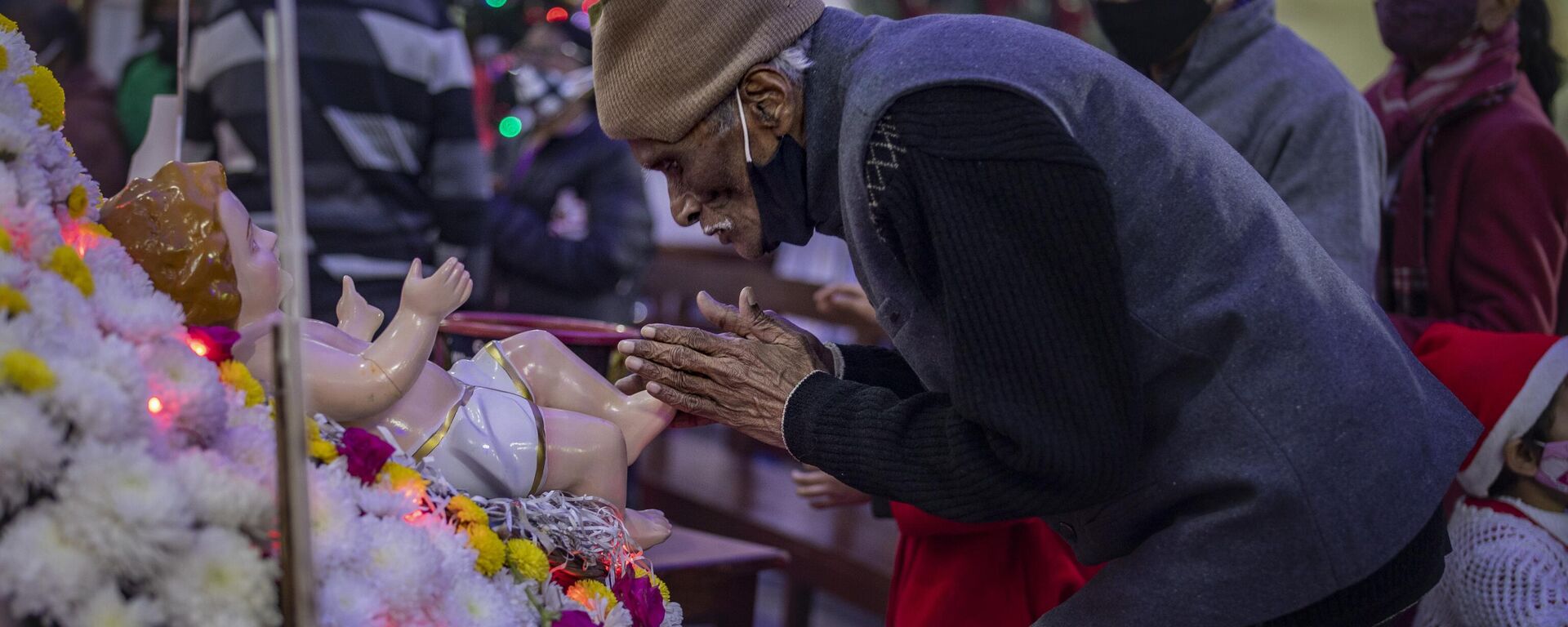 An elderly Indian Christian man touches the feet of the statue of baby Jesus after attending a Christmas mass at Saint Mary's church in Noida, a suburb of New Delhi, India, Saturday, Dec. 25, 2021. - Sputnik भारत, 1920, 13.12.2022