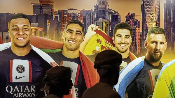 People passing a painting of PSG soccer players Kylian Mbappe, Achraf Hakimi, Carlos Soler and Lionel Messi on a wall during the Soccer World Cup in central Doha, Qatar, on Monday, Dec. 12, 2022. - Sputnik India