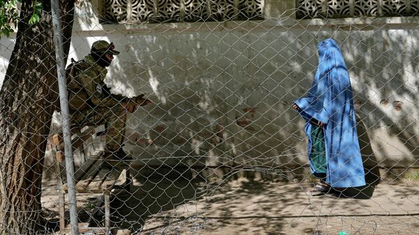 A Taliban fighter stands guard as a woman enters the government passport office, in Kabul, Afghanistan, Wednesday, April 27, 2022. Afghanistan's Taliban leadership has ordered all Afghan women to wear the all-covering burqa in public.  - Sputnik भारत