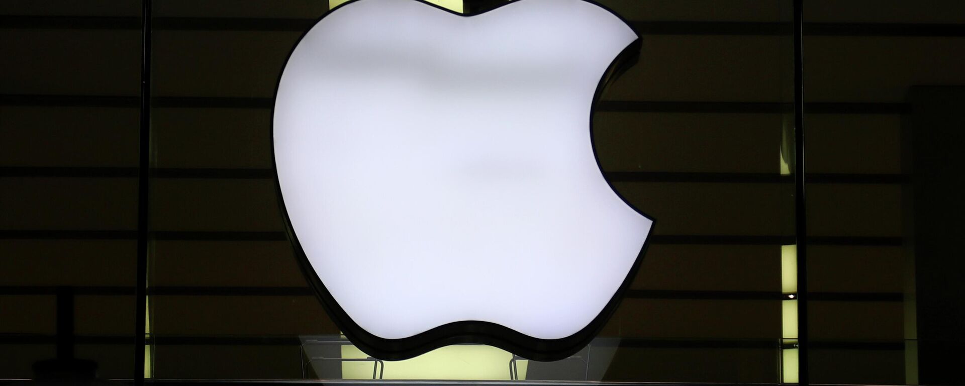 In this Wednesday, Dec. 16, 2020 file photo, the logo of Apple is illuminated at a store in the city center in Munich, Germany. Apple said late Wednesday Sept. 1, 2021, it is relaxing rules to allow some app developers such as Spotify, Netflix and digital publishers to include an outside link so users can sign up for paid subscription accounts.  - Sputnik India, 1920, 25.09.2023