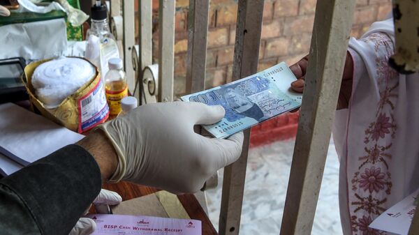 A woman (R) gets rupee notes as she collects cash of financial assistance through a district administration counter under the governmental Ehsaas Emergency Cash Programme for families in need during a government-imposed nationwide lockdown as a preventive measure against the COVID-19 coronavirus, in Peshawar on April 9, 2020 - Sputnik India
