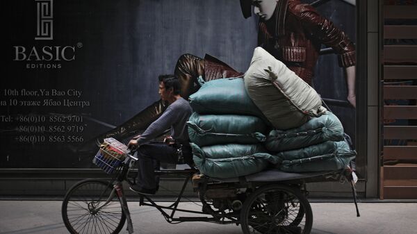 Мужчина едет на трехколесном велосипеде, нагруженном товарами, мимо рекламного щита у Международного торгового центра Ritan в Пекине  - Sputnik भारत