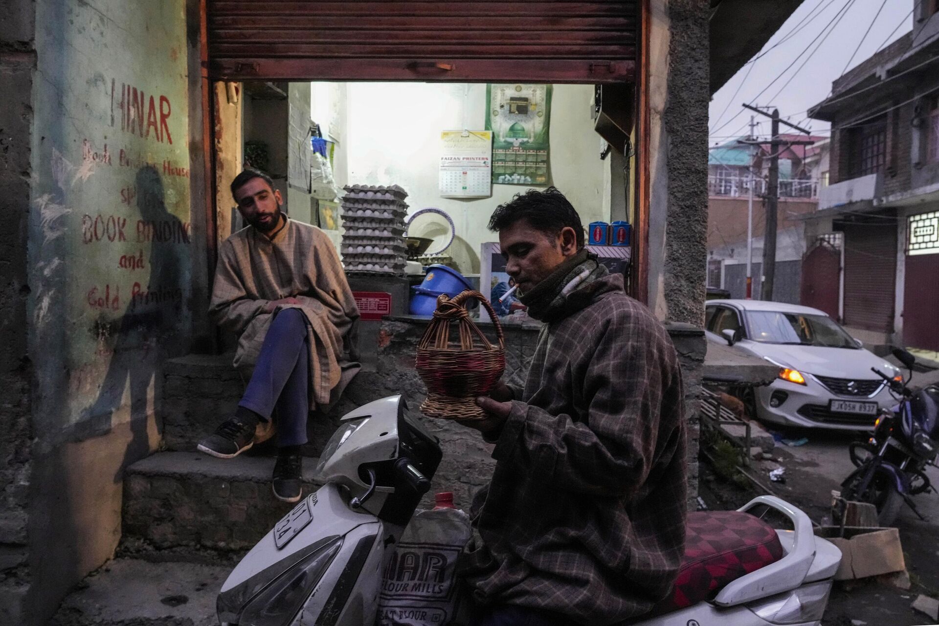 A Kashmiri man lights a cigarette using a fire pot as a shopkeeper waits for customers on a cold evening in Srinagar, Sunday, Jan. 8, 2023. - Sputnik India, 1920, 06.02.2023