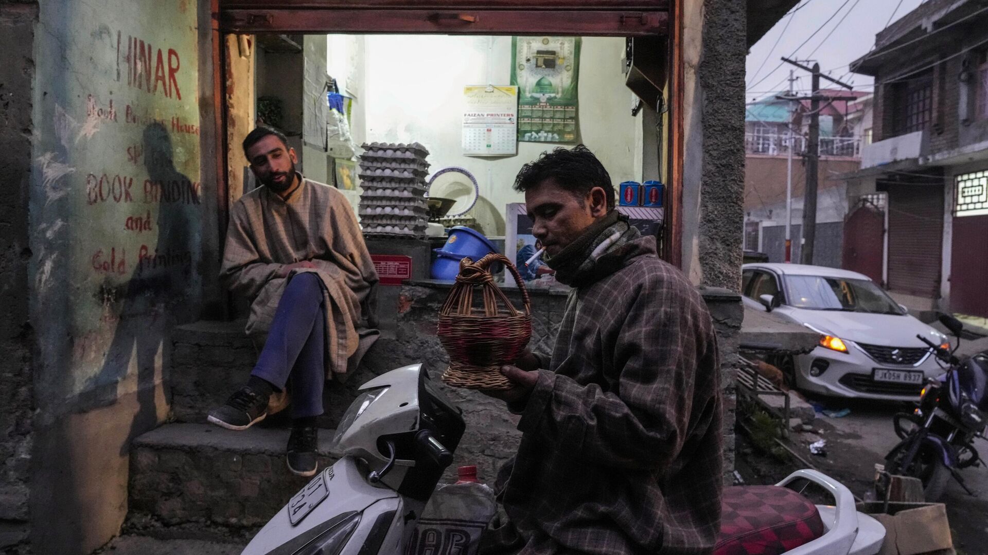 A Kashmiri man lights a cigarette using a fire pot as a shopkeeper waits for customers on a cold evening in Srinagar, Sunday, Jan. 8, 2023. - Sputnik India, 1920, 17.01.2023