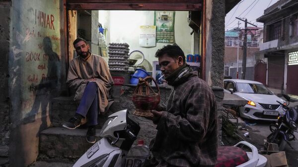 A Kashmiri man lights a cigarette using a fire pot as a shopkeeper waits for customers on a cold evening in Srinagar, Sunday, Jan. 8, 2023. - Sputnik India