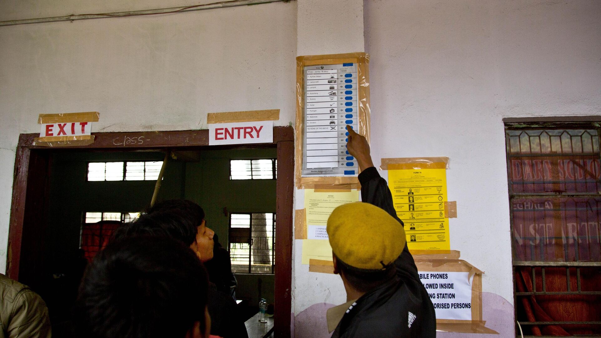 An Indian security person demonstrates to a voter standing in queue how to cast vote on a model of an electronic voting machine displayed outside a polling station during the Meghalaya state assembly election in Nongpoh, India, Tuesday, Feb. 27, 2018. - Sputnik India, 1920, 18.01.2023