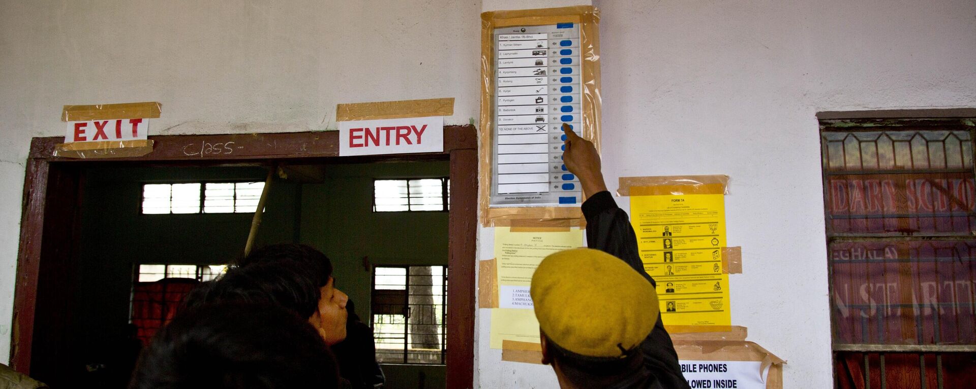 An Indian security person demonstrates to a voter standing in queue how to cast vote on a model of an electronic voting machine displayed outside a polling station during the Meghalaya state assembly election in Nongpoh, India, Tuesday, Feb. 27, 2018. - Sputnik India, 1920, 29.05.2023