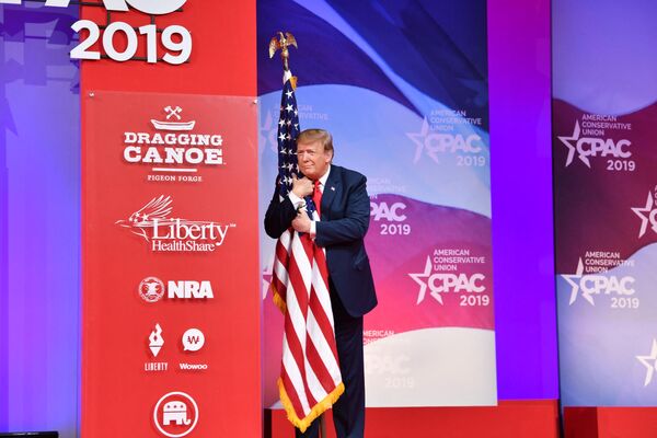 Former US President Donald Trump hugs the US flag as he arrives to speak at the annual Conservative Political Action Conference (CPAC) in National Harbor, Maryland, on March 2, 2019. (Photo by Nicholas Kamm / AFP) - Sputnik India