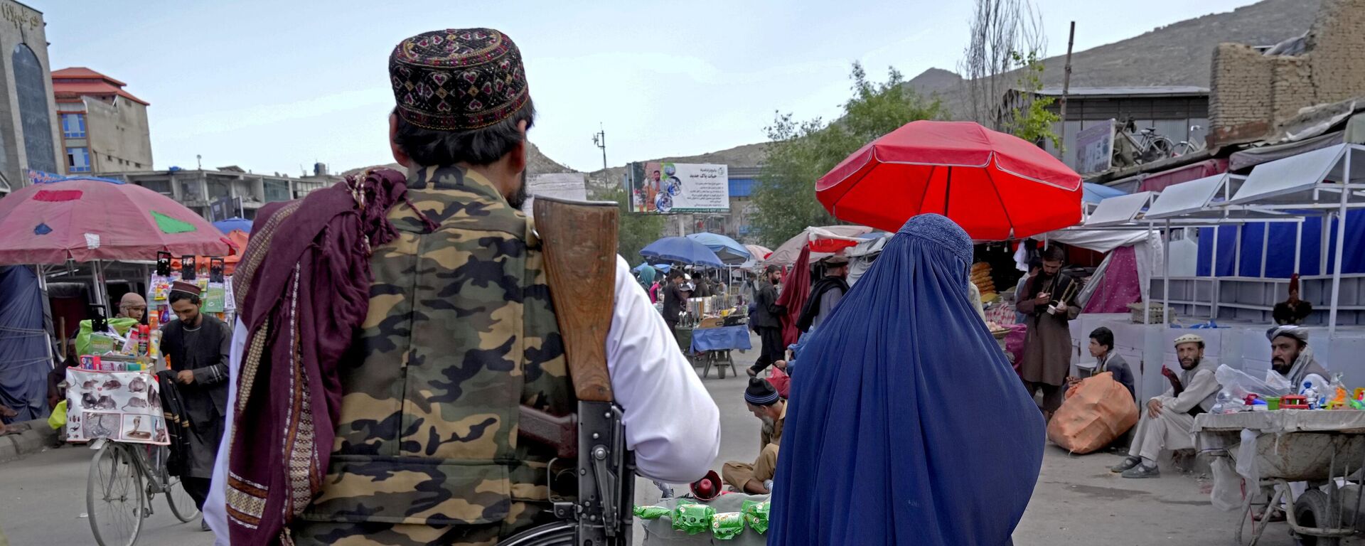 A woman wearing a burka walks through the old market as a Taliban fighter stands guard, in downtown Kabul, Afghanistan, Sunday, May 8, 2022. - Sputnik भारत, 1920, 08.08.2023