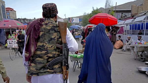 A woman wearing a burka walks through the old market as a Taliban fighter stands guard, in downtown Kabul, Afghanistan, Sunday, May 8, 2022. - Sputnik भारत