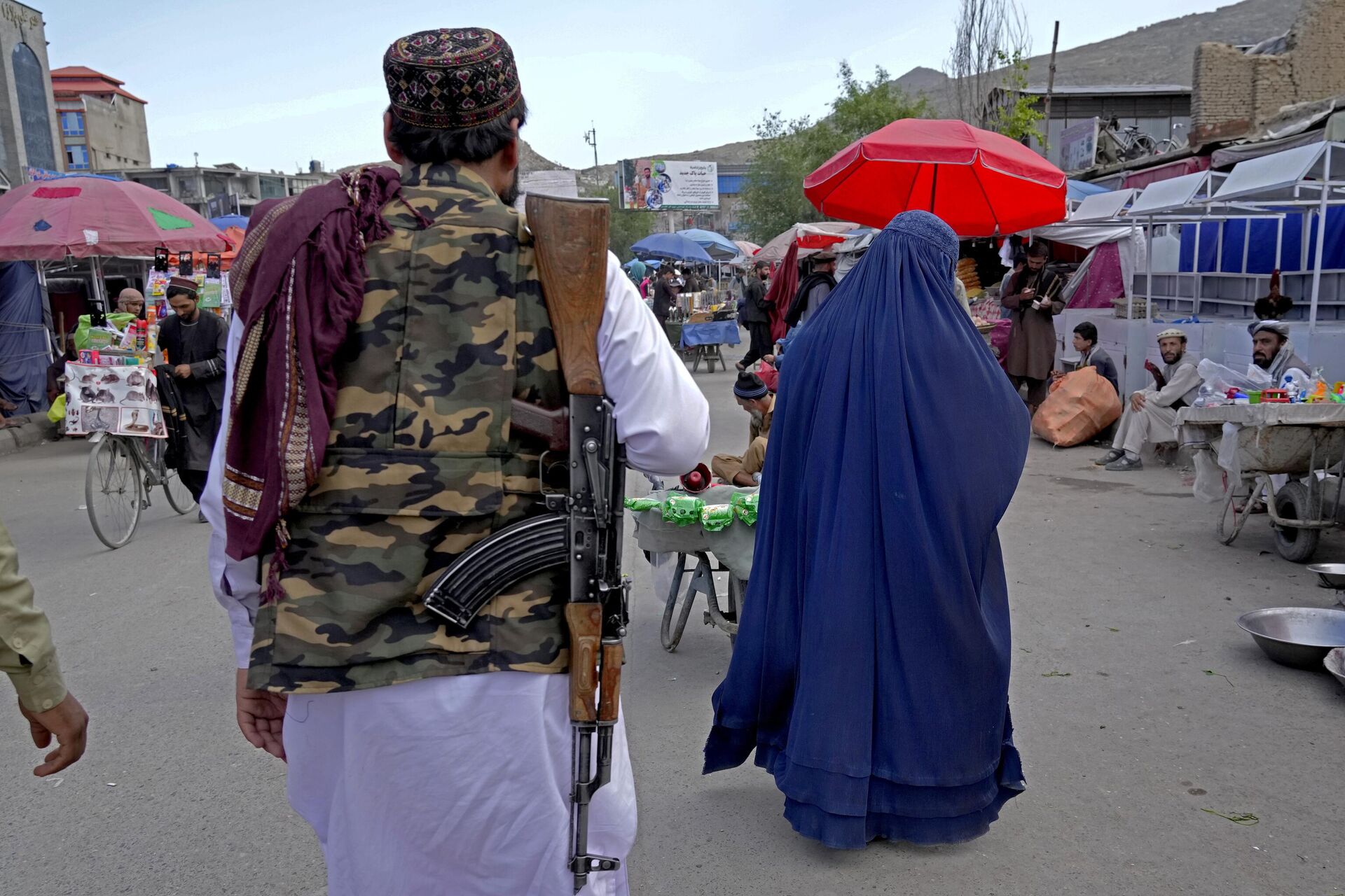A woman wearing a burka walks through the old market as a Taliban fighter stands guard, in downtown Kabul, Afghanistan, Sunday, May 8, 2022. - Sputnik India, 1920, 29.01.2023