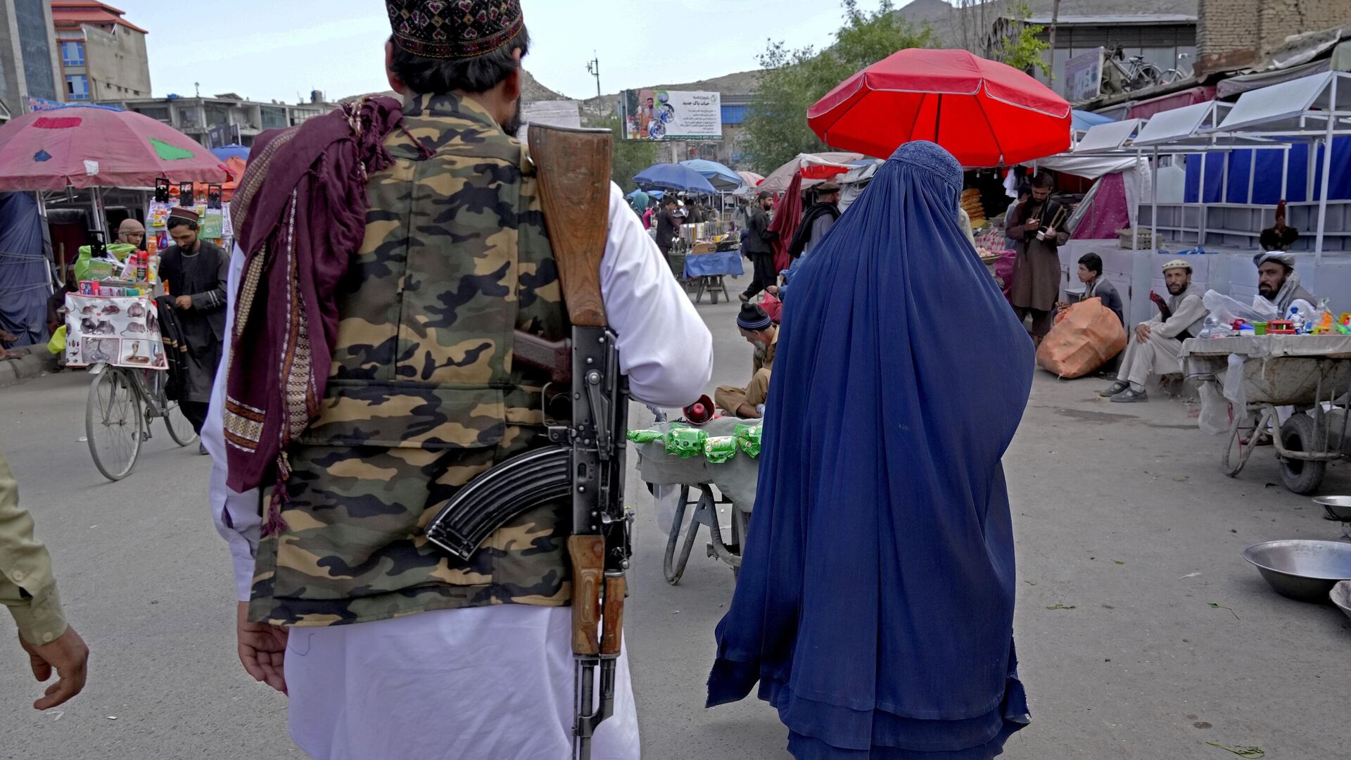A woman wearing a burka walks through the old market as a Taliban fighter stands guard, in downtown Kabul, Afghanistan, Sunday, May 8, 2022. - Sputnik India, 1920, 20.01.2023