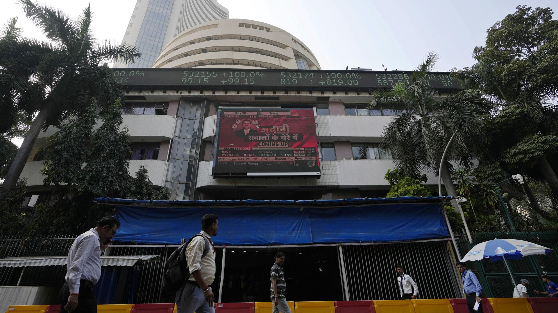 People walk past an electronic display featuring news about Adani Group outside the Bombay Stock Exchange building in Mumbai, India, Friday, Jan. 27, 2023. - Sputnik India, 1920, 22.05.2023