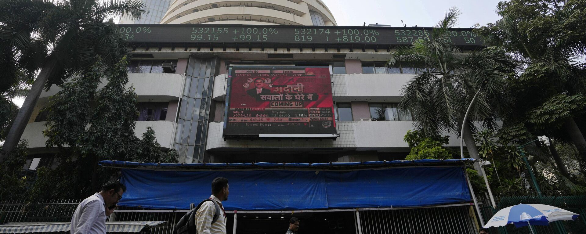 People walk past an electronic display featuring news about Adani Group outside the Bombay Stock Exchange building in Mumbai, India, Friday, Jan. 27, 2023. - Sputnik India, 1920, 02.02.2023