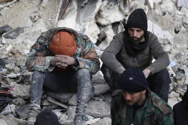 People react as they sit on the wreckage of collapsed buildings, in Aleppo, Syria, Tuesday, Feb. 7, 2023. - Sputnik India