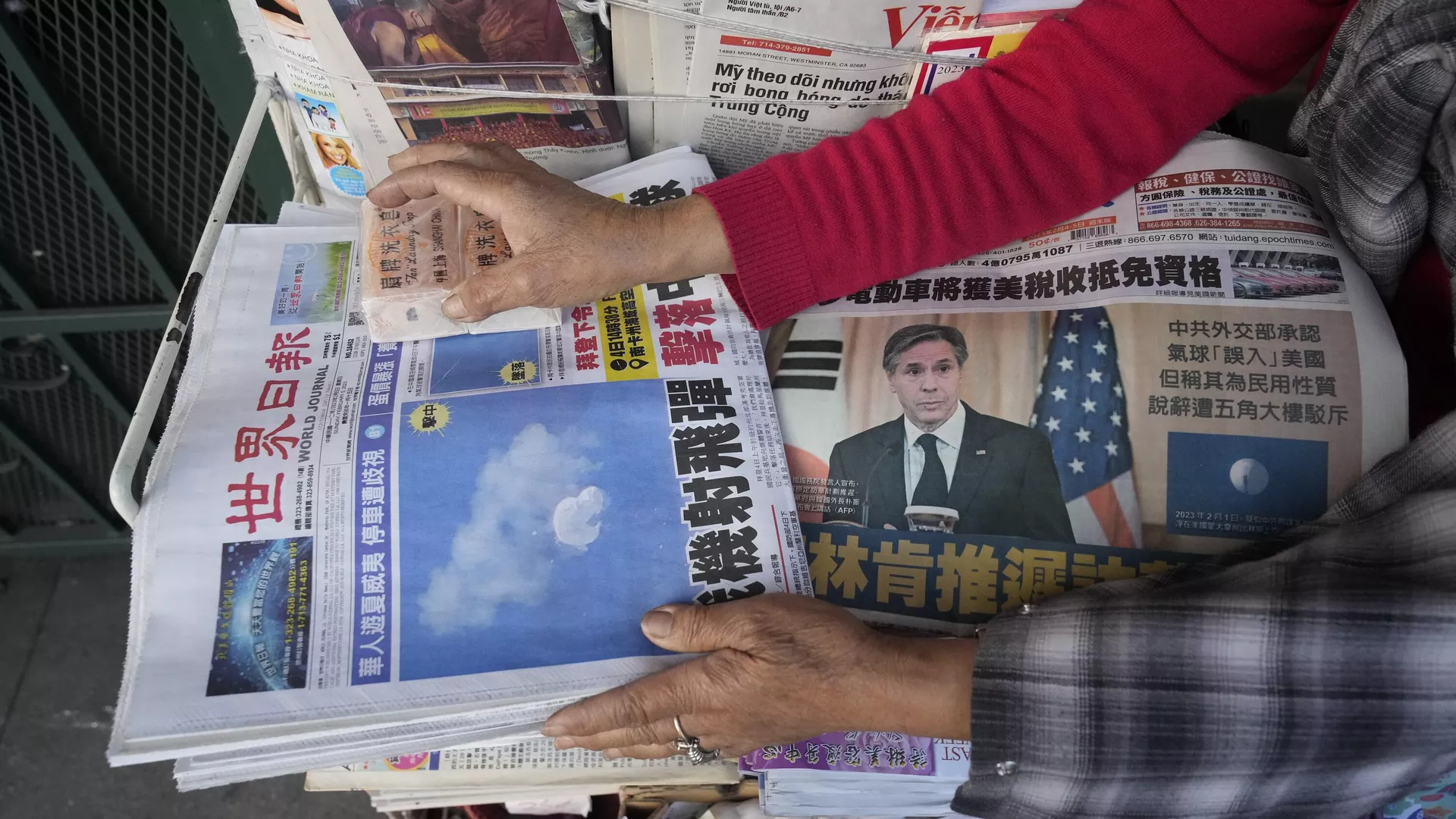 Business owner Annie weights down copies of the Chinese Daily News newspaper showcasing pictures of a suspected Chinese spy balloon, in the Chinatown district of Los Angeles Sunday, Feb. 5, 2023.