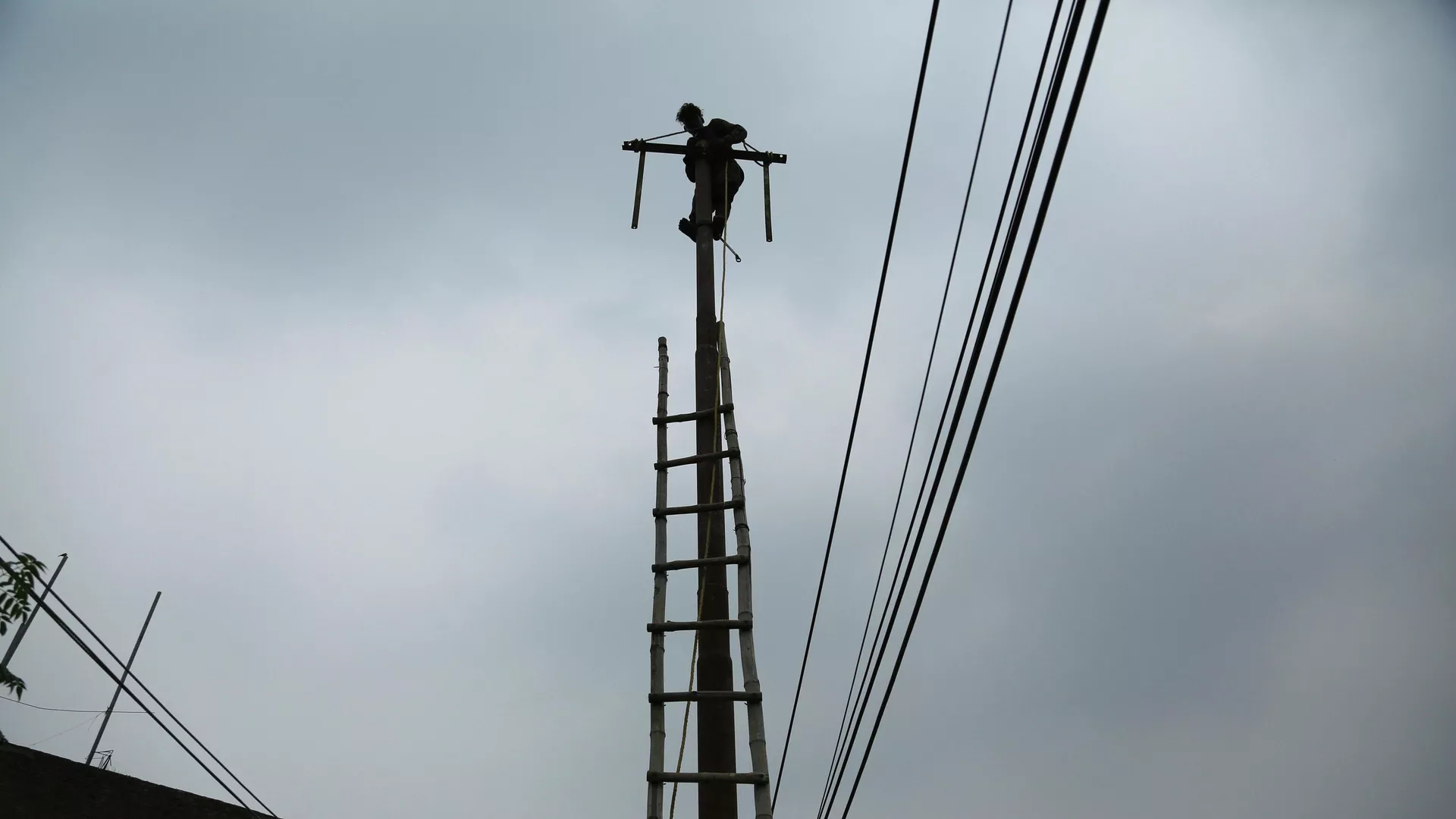 An Indian electricity department worker climbs on a pole to fix power lines as monsoon clouds gather above in Jammu, India, Sunday, July 18, 2021