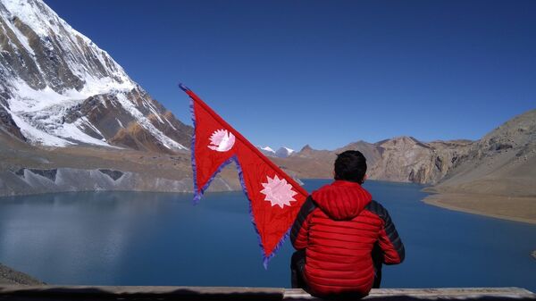   Man sitting on the shore of Tilicho Lake in Nepal, holding flag - Sputnik India