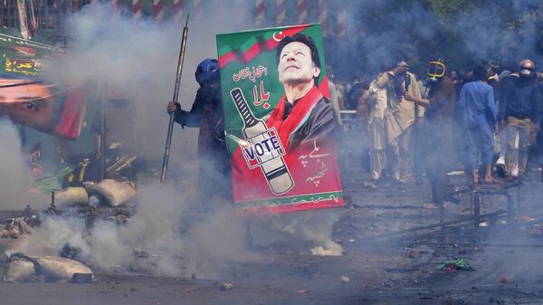 Supporters of former Prime Minister Imran Khan take cover after riot police officers fire tear gas to disperse them during clashes in Lahore, Pakistan, Wednesday, March 15, 2023. - Sputnik India