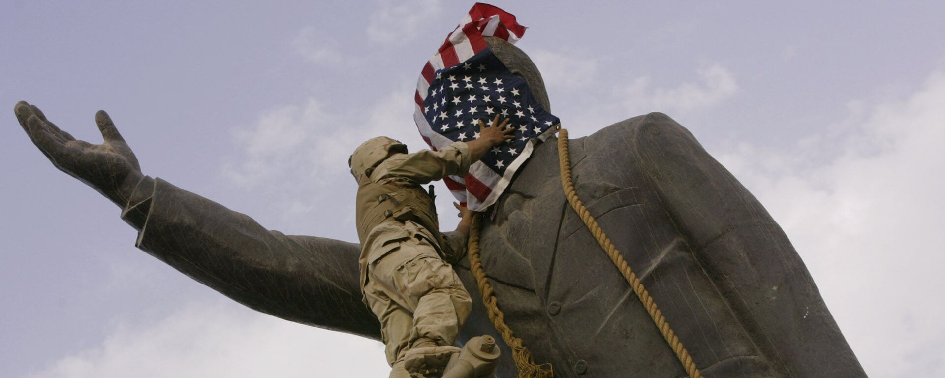 In this file photo taken Wednesday, April 9, 2003, an Iraqi man, bottom right, watches Cpl. Edward Chin of the 3rd Battalion, 4th Marines Regiment, cover the face of a statue of Saddam Hussein with an American flag before toppling the statue in downtown in Baghdad, Iraq. - Sputnik भारत, 1920, 20.03.2023