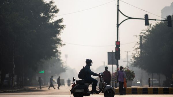 A man wearing a facemask rides his scooter along a street amid smoggy condition in New Delhi on October 30, 2020. - Sputnik भारत