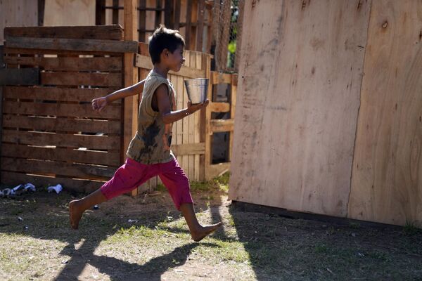 A child, who was displaced from his home by the rising waters of the Paraguay River, runs past carrying a container filled with water, on the grounds of his temporary shelter, in Asuncion, Paraguay, Saturday, March 18, 2023. - Sputnik भारत