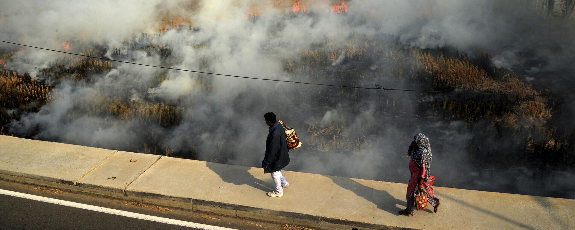 A couple walks past crop stubble set on fire by farmers on the out skirts of Jalandhar, in the northern Indian state of Punjab, Wednesday, Nov. 17, 2021. - Sputnik India, 1920, 28.03.2023