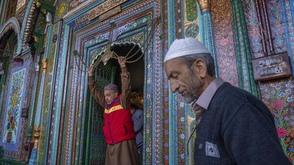 A Kashmiri man, left, touches in reverence a chain at the entrance to the shrine of Shah-e-Hamadan as he leaves after offering prayers on the third Friday of Ramadan in Srinagar, Friday, April 7, 2023. - Sputnik India