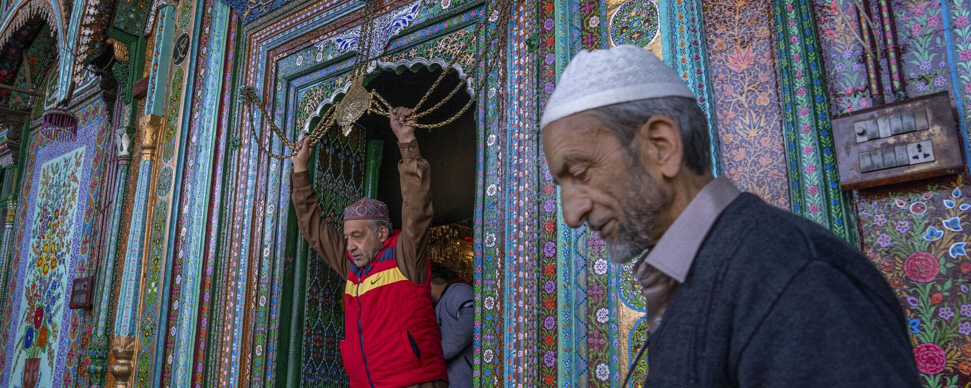 A Kashmiri man, left, touches in reverence a chain at the entrance to the shrine of Shah-e-Hamadan as he leaves after offering prayers on the third Friday of Ramadan in Srinagar, Friday, April 7, 2023. - Sputnik India, 1920, 04.06.2023