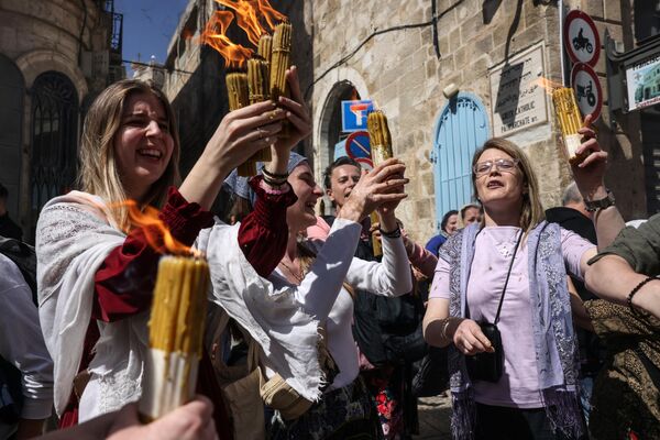 ईसाई लोग जेरूसलेम में पवित्र दरगाह वाले चर्च से पवित्र अग्नि की मदद से जली मोमबत्तियाँ लेकर इस चर्च के पास खड़े हैं (Photo by AHMAD GHARABLI / AFP) - Sputnik भारत