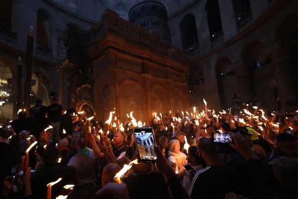 ऑर्थडाक्स ईसाई 15 अप्रैल, 2023 को पवित्र दरगाह वाले चर्च में पवित्र अग्नि के समारोह के दौरान एडिकुले के पास जली मोमबत्तियाँ लेकर खड़े हैं, जिसे पारंपरिक रूप से ईसा मसीह का समाधि स्थल माना जाता है (Photo by Menahem KAHANA / AFP) - Sputnik भारत