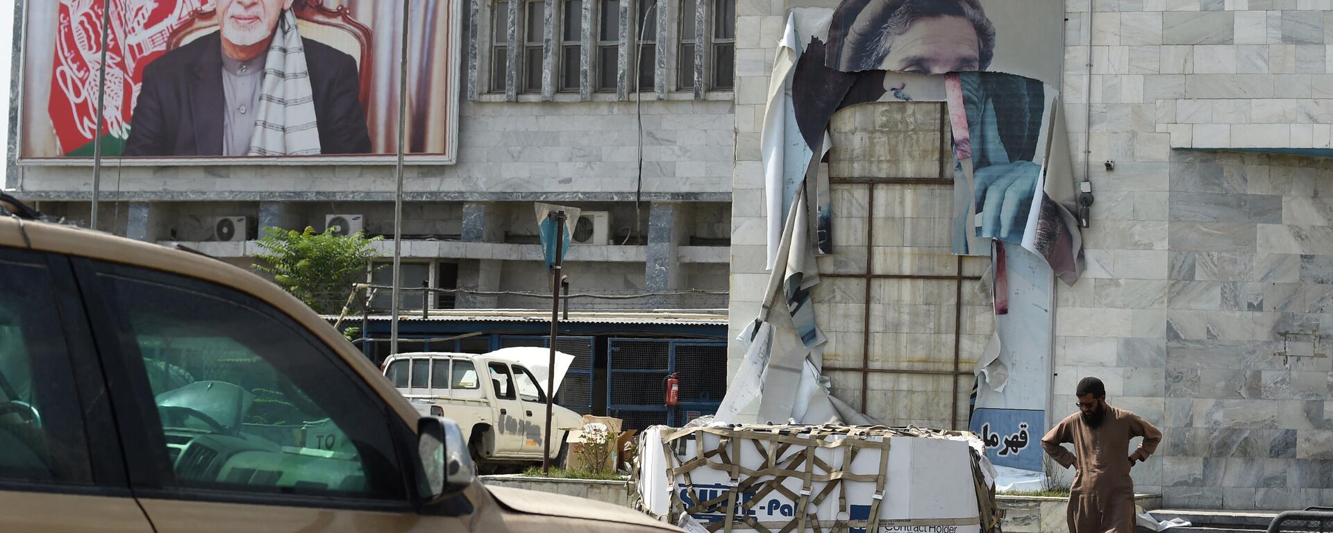 A Taliban fighter walks near a torn down banner of late Afghan Mujahideen leader Ahmed Shah Massoud (R) and a poster of former Afghan president Ashraf Ghani (L), who fled the country during the recent Taliban military takeover of Aghanistan, at the airport in Kabul on August 31, 2021 - Sputnik India, 1920, 12.05.2023