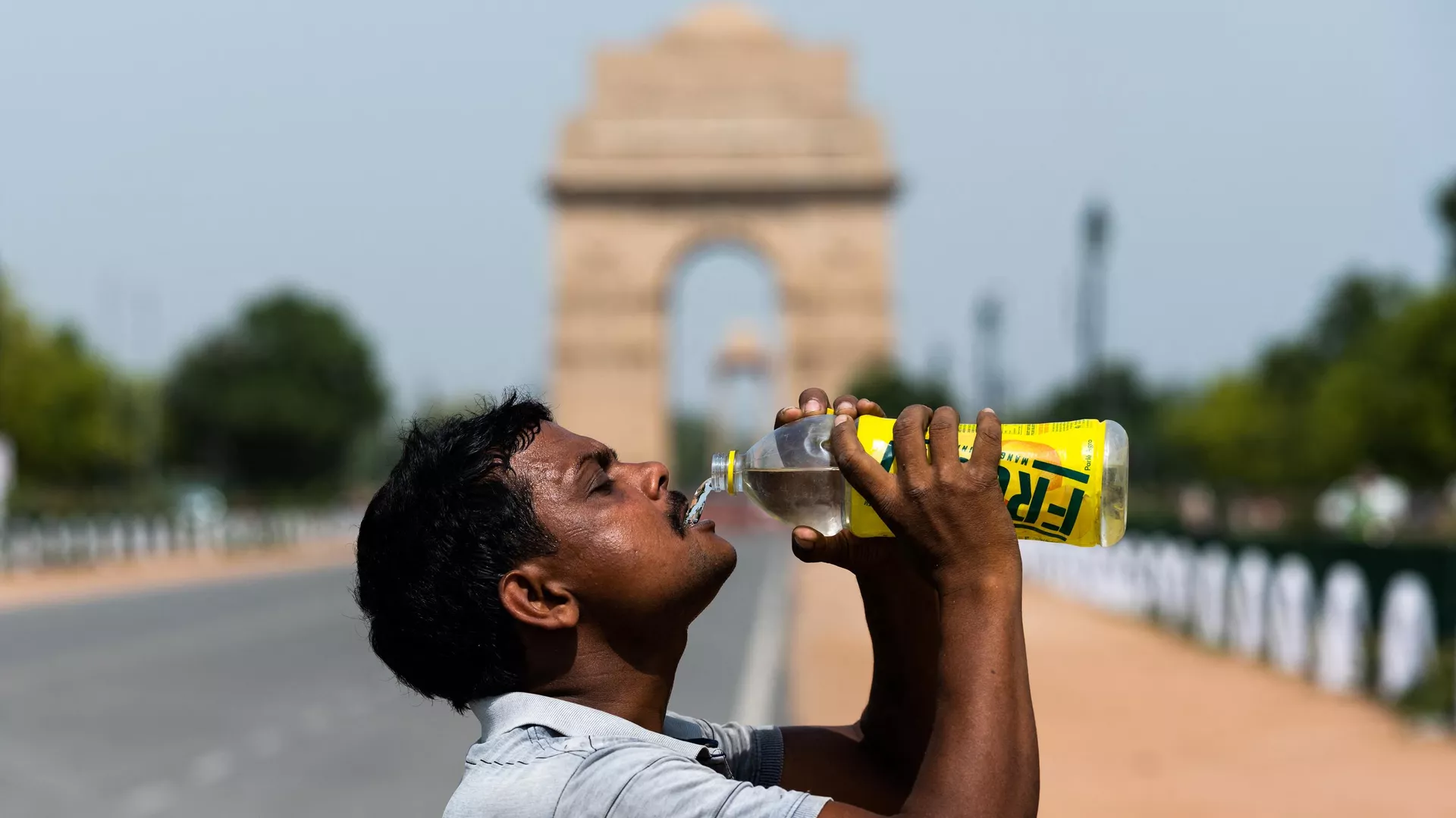 A worker quenches his thirst with water from a bottle taking a break from cleaning weeds from a park near India Gate amid rising temperatures in New Delhi on May 27, 2020.