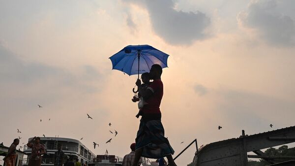 A man carrying his son walks with an umbrella during a heatwave in Yangon on April 19, 2023. - Sputnik India
