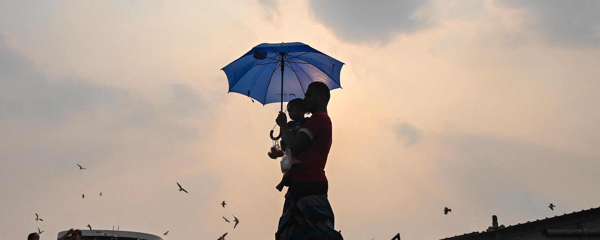 A man carrying his son walks with an umbrella during a heatwave in Yangon on April 19, 2023. - Sputnik India, 1920, 21.04.2023