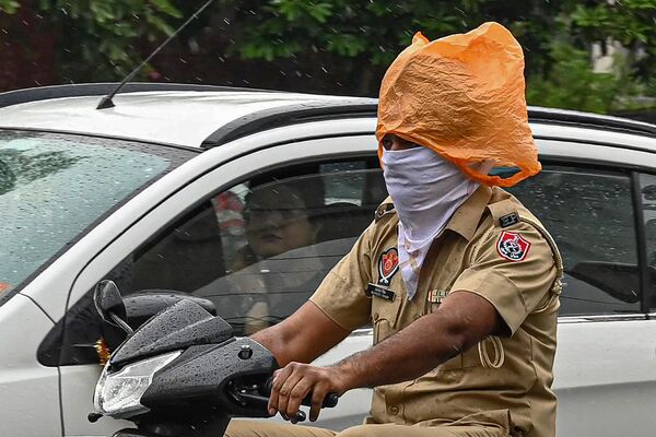 A policeman covers his head with a plastic bag amid light drizzle in Amritsar on May 1, 2023.  - Sputnik India