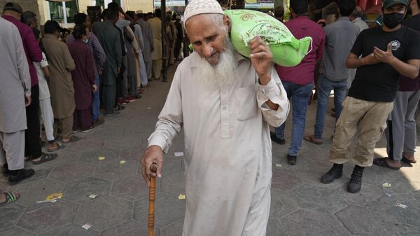 A police officer stands guard while an elderly man leaves after getting a free sack of wheat flour at a distribution point, in Lahore, Pakistan, Thursday, March 30, 2023. - Sputnik India