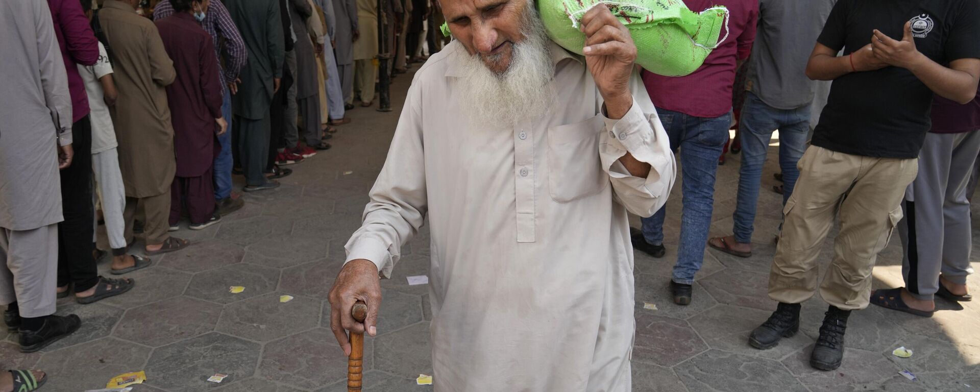 A police officer stands guard while an elderly man leaves after getting a free sack of wheat flour at a distribution point, in Lahore, Pakistan, Thursday, March 30, 2023. - Sputnik India, 1920, 03.05.2023