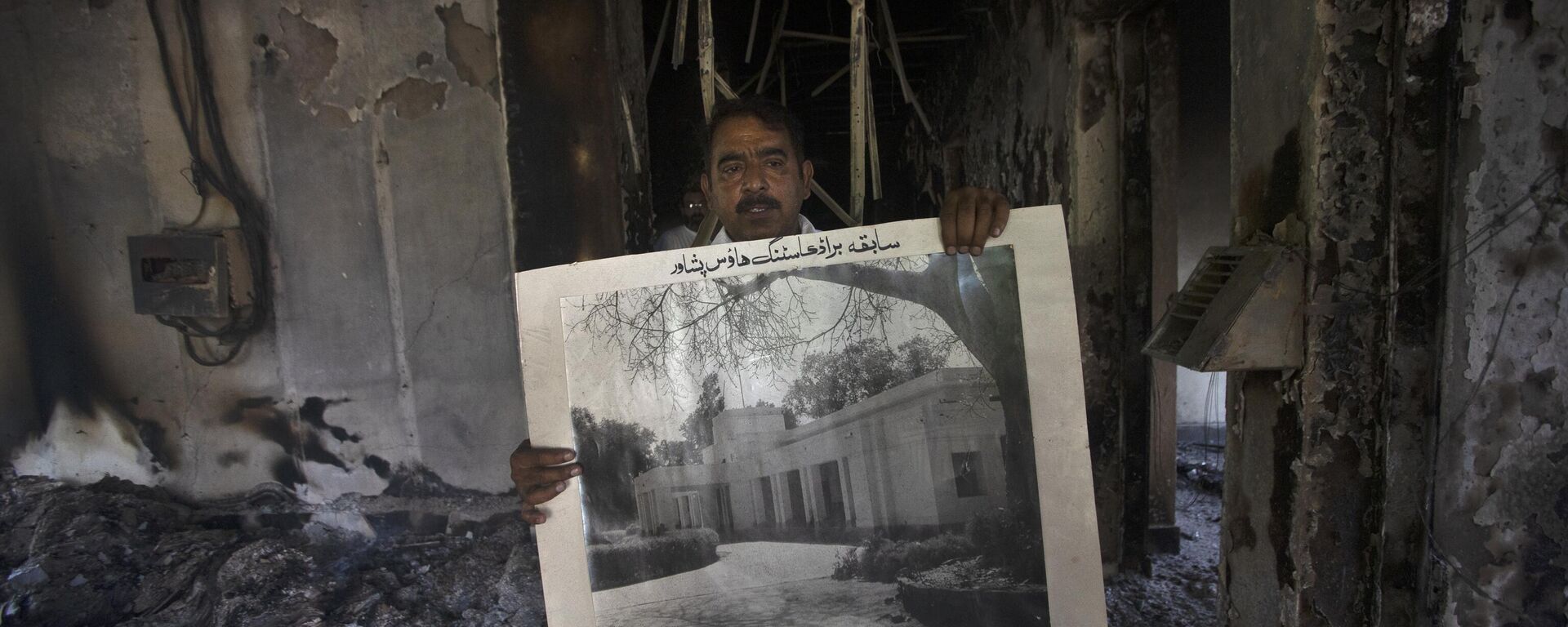 A government employee displays an old picture to media members inside the Radio Pakistan building burnt in the Wednesday's clashes between police and the supporters of Pakistan's former Prime Minister Imran Khan, in Peshawar, Pakistan, Thursday, May 11, 2023. - Sputnik India, 1920, 11.05.2023