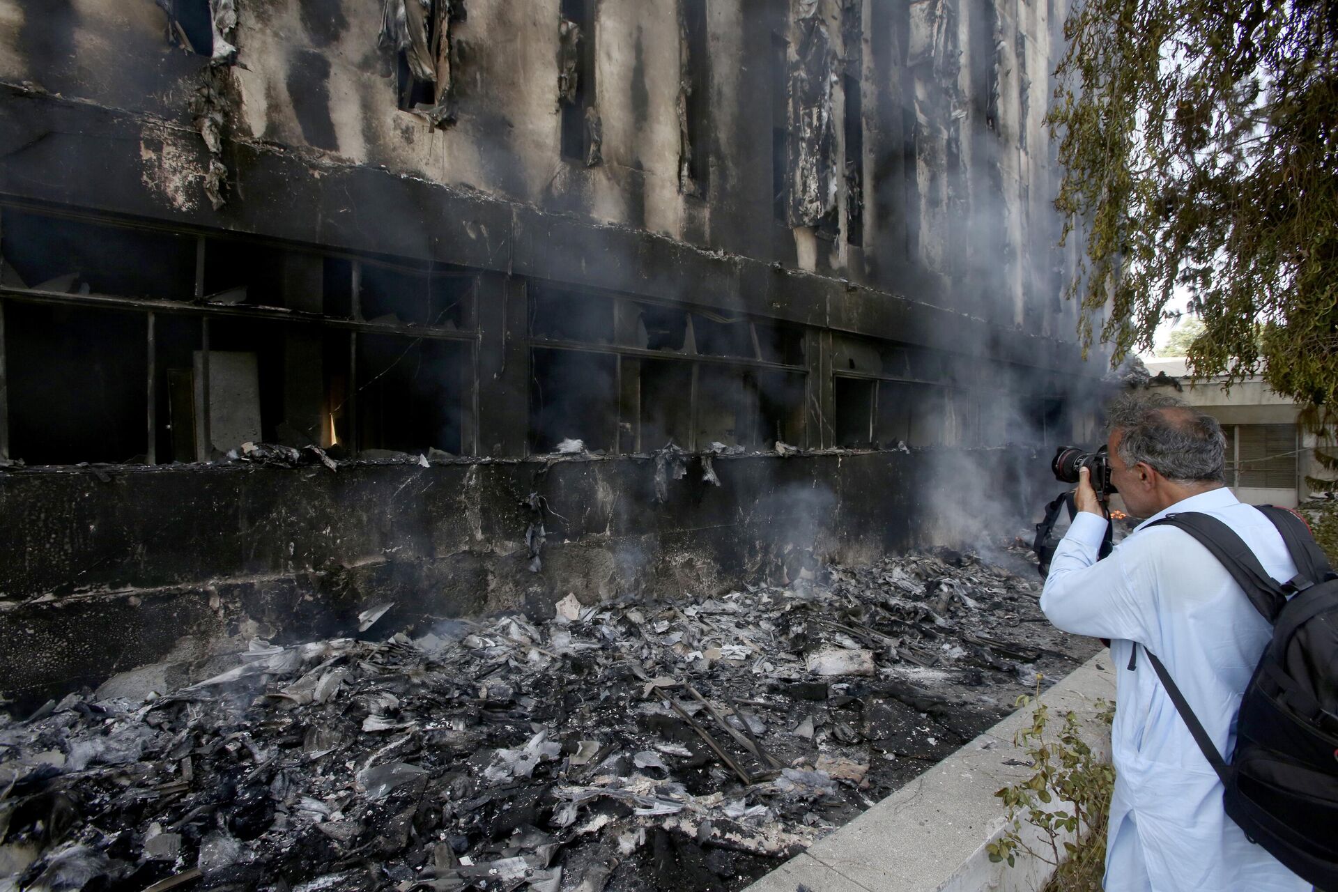 A member of media takes a photo of a burning building of the Radio Pakistan that was set on fire by angry supporters of Pakistan's former Prime Minister Imran Khan protesting against the arrest of their leader, in Peshawar, Pakistan, Wednesday, May 10, 2023. - Sputnik India, 1920, 11.05.2023