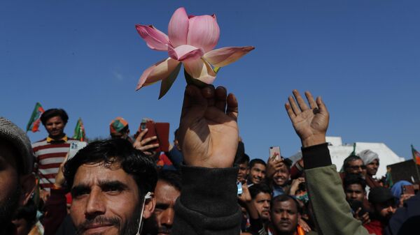 A supporter holds a lotus flower, the symbol of India's ruling Bharatiya Janata Party (BJP) as they listen to Uttar Pradesh Chief Minister Yogi Adityanath during an election rally in Shamli, India, Saturday, Feb. 5, 2022.  - Sputnik India