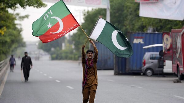 A supporter of Pakistan's former Prime Minister Imran Khan holds flags near his house, in Lahore, Pakistan, Wednesday, May 17, 2023. - Sputnik भारत