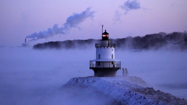 Spring Point Ledge Light is surrounded by arctic sea smoke while emissions from the Wyman Power plant, background, are blown horizontal by the fierce wind, Saturday, Feb. 4, 2023, in South Portland, Maine. - Sputnik India