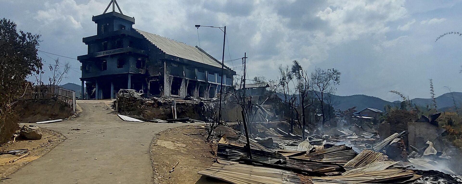 The remains of a burnt church (L) and houses (R) are seen in Langching village some 45 km from Imphal on May 31, 2023, during ongoing ethnic violence in India's northeastern Manipur state. - Sputnik भारत, 1920, 21.06.2023