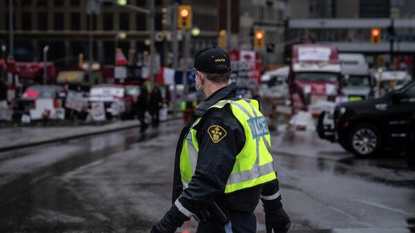 An Ontario Provincial Police officer walks in front of a row of trucks parked on the street near the Canadian parliament building in Ottawa on Thursday, Feb. 17, 2022. Hundreds of truckers clogging the streets of Canada's capital city in a protest against COVID-19 restrictions are bracing for a possible police crackdown. (AP Photo/Robert Bumsted) - Sputnik भारत