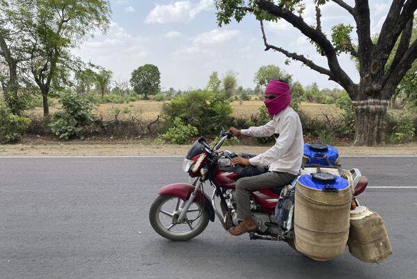 एक दूधवाला अपनी मोटरसाइकिल चला रहा है । दूध को खराब होने से बचाने के लिए उनके कंटेनर को जूट की गीली बोरियों से ढक दिया गया है। (AP Photo/Rajesh Kumar Singh) - Sputnik भारत