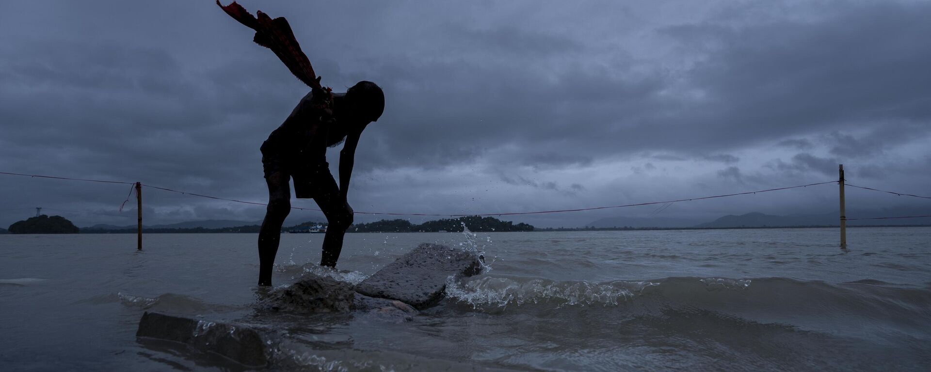 A man washes his clothes in the river Brahmaputra as rain clouds hover over in Guwahati, northeastern Assam state, India, Tuesday, Oct. 25, 2022. - Sputnik India, 1920, 22.06.2023