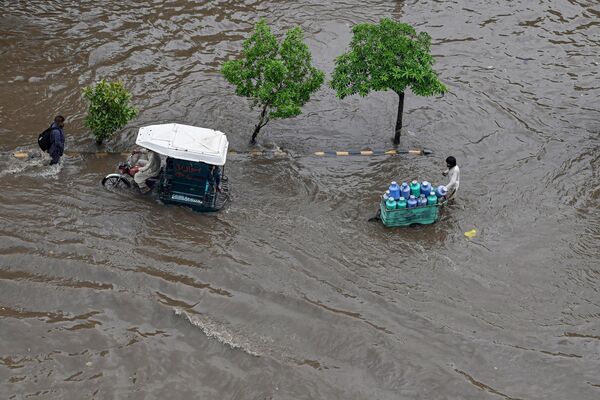 लाहौर में भारी बारिश के बाद लोग जलमग्न सड़क पर चल रहे हैं, जून 26, 2023. (Photo by Arif ALI / AFP) - Sputnik भारत