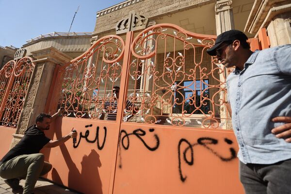 बगदाद में स्वीडिश दूतावास के प्रवेश द्वार पर भित्तिचित्रों का छिड़काव करता व्यक्ति (Photo by Ahmad AL-RUBAYE / AFP) - Sputnik भारत