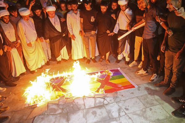 LGBTQ+ झंडे के साथ पोस्टर को जलाते इराकी शिया मौलवी मुक्तदा अस-सद्र के समर्थक (Photo by Mohammed SAWAF / AFP) - Sputnik भारत